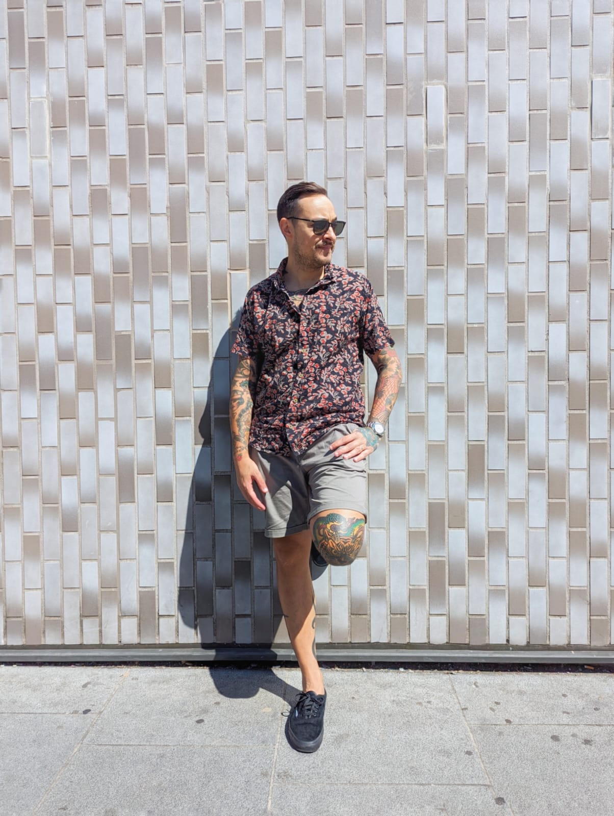 Male model with glasses and tatoo posing in a black and red floral shirt.