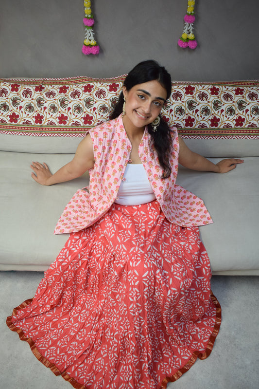 Girl smiling wearing a vest and skirt on a cream sofa with floral handing on the back wall.